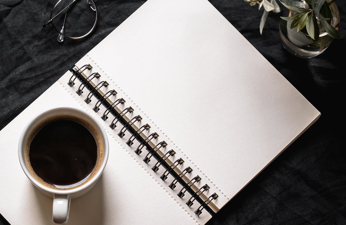 An open blank journal with a coffee cup, plant, and glasses nearby — symbolizing a fresh start and reflective wellness reset.
