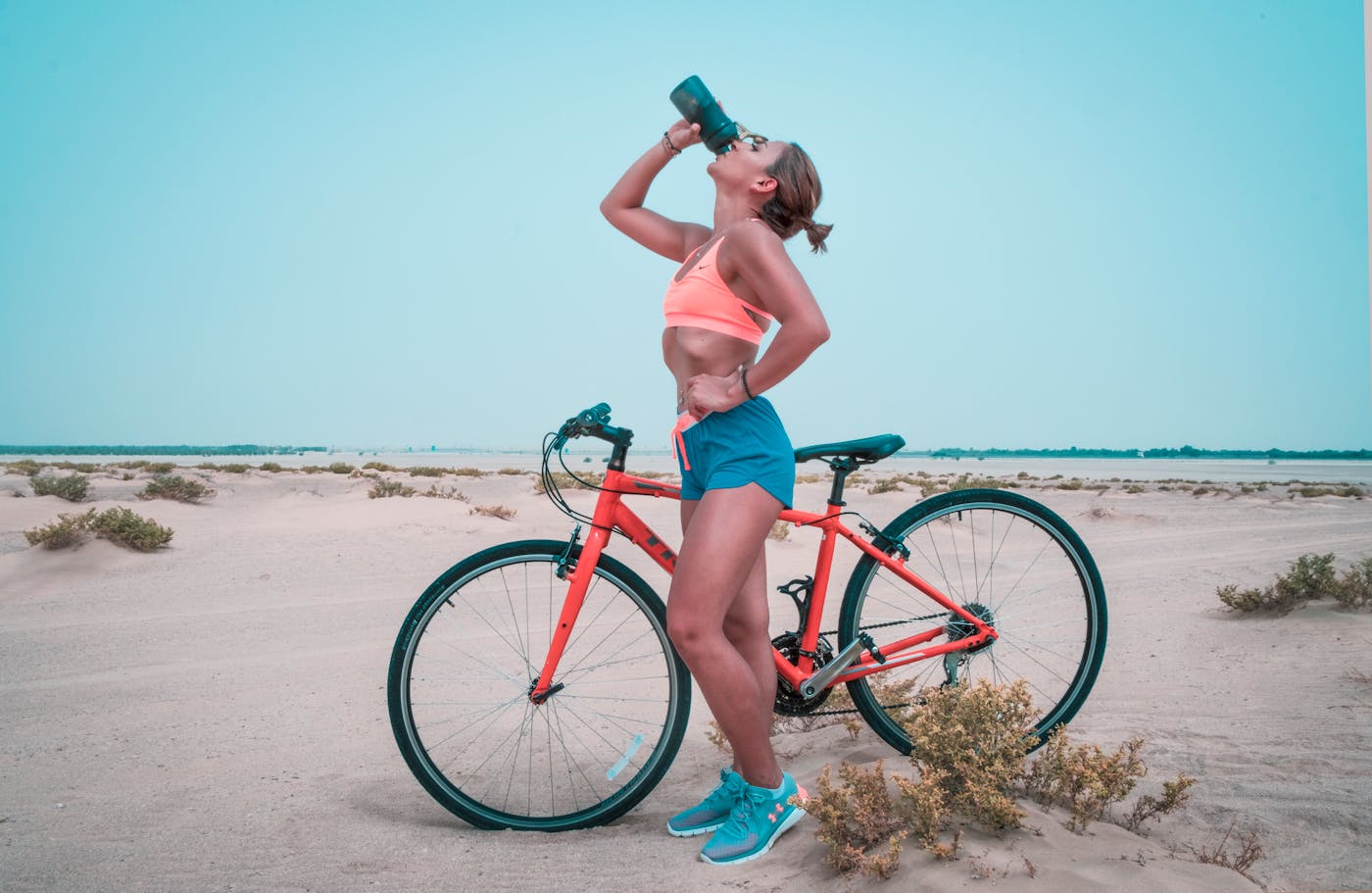 Confident athletic woman in workout gear hydrating next to a bike in a bright outdoor setting – symbolizing clarity, momentum, and personalized fitness